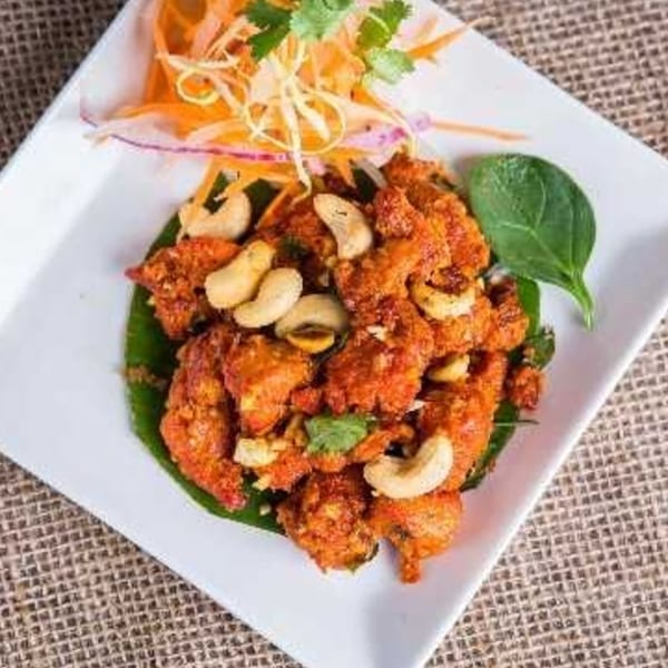 Peppers Indian Cuisine's orange chicken dish with cashews, garnished with shredded vegetables and cilantro.