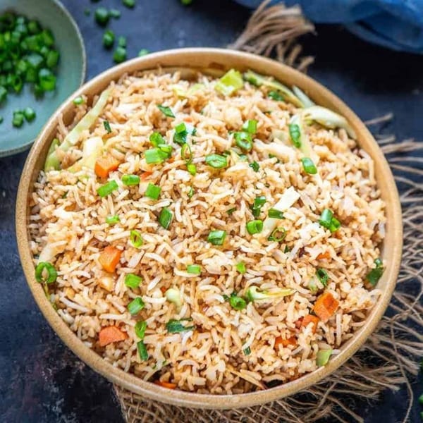 A wooden bowl filled with Indian fried rice, garnished with chopped green onions and vegetables.