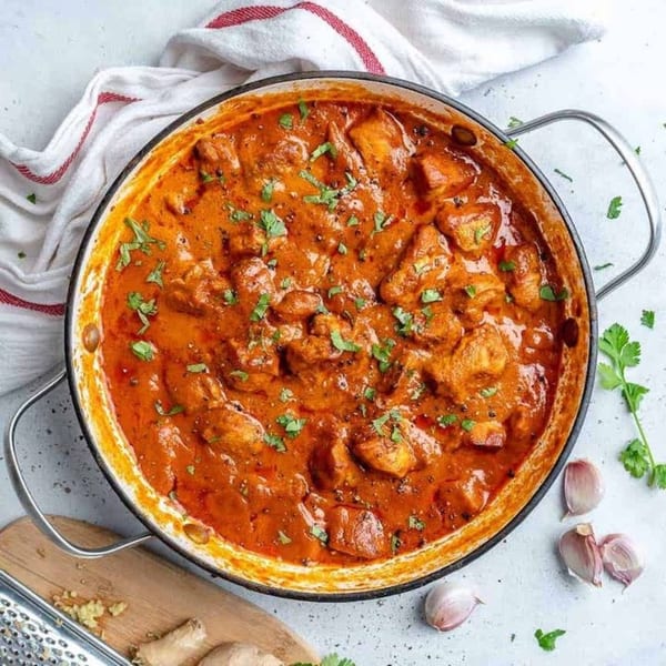 A cast iron pan filled with rich orange Indian butter chicken, garnished with fresh cilantro.