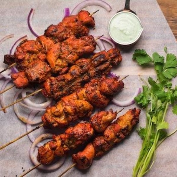 Indian chicken tikka skewers with red onions, cilantro, and a side of green dipping sauce.