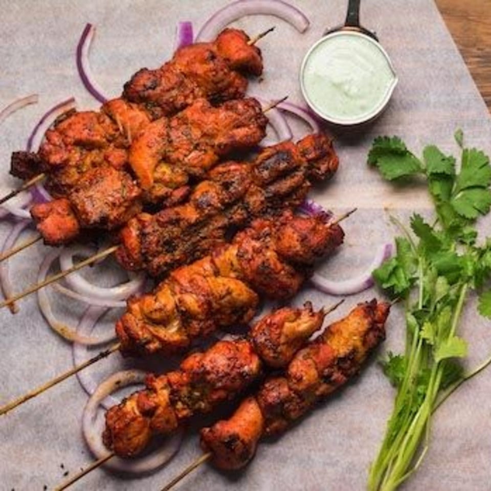Indian chicken tikka skewers with red onions, cilantro, and a side of green dipping sauce.