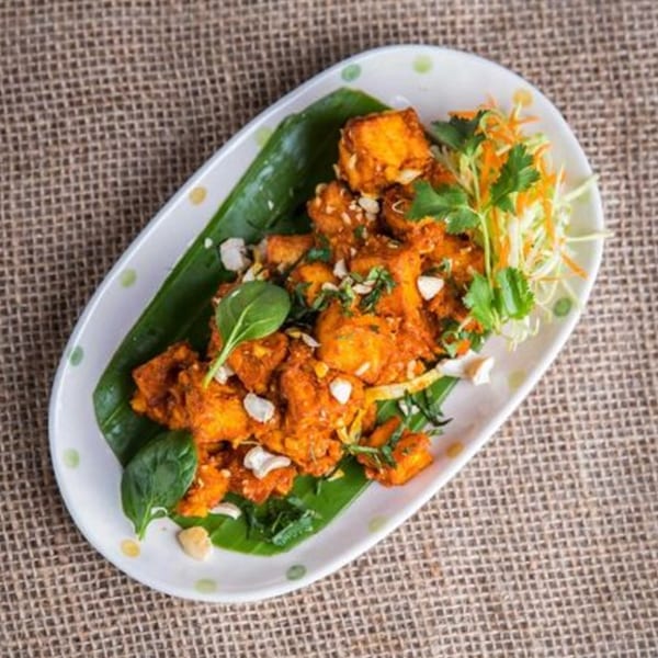 Peppers Indian Cuisine's orange chicken dish, garnished with nuts, cilantro, and shredded vegetables.