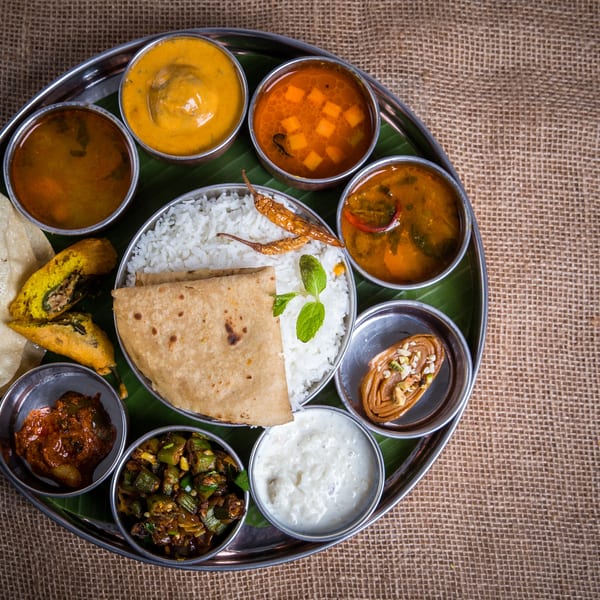 A traditional Indian thali with rice, roti, curries, raita, and fried snacks on a banana leaf.