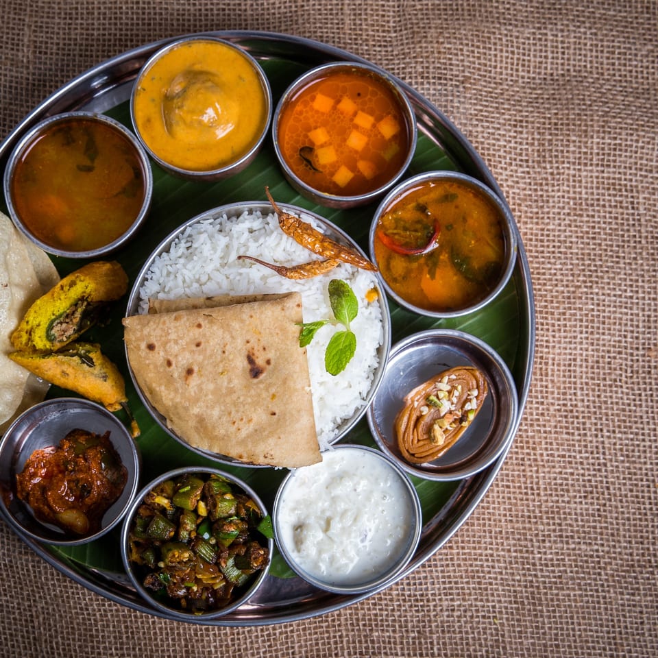 A traditional Indian thali with rice, roti, curries, raita, and fried snacks on a banana leaf.