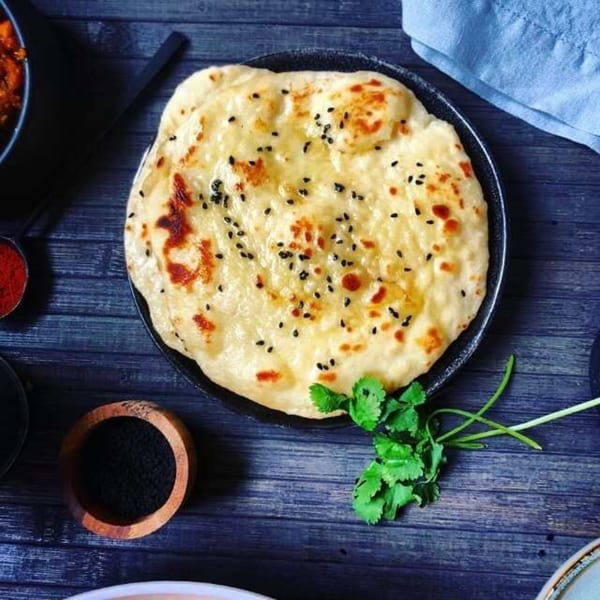 A plate of golden naan bread topped with black sesame seeds and fresh cilantro.