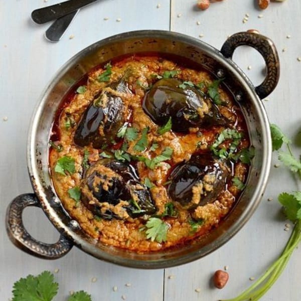 A metal bowl of Indian eggplant curry with a rich, creamy sauce and fresh cilantro.