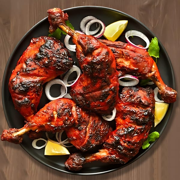 A black plate filled with several pieces of grilled Indian tandoori chicken, garnished with onions and lemon wedges.