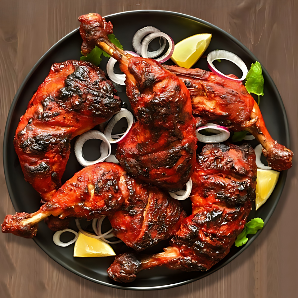 A black plate filled with several pieces of grilled Indian tandoori chicken, garnished with onions and lemon wedges.
