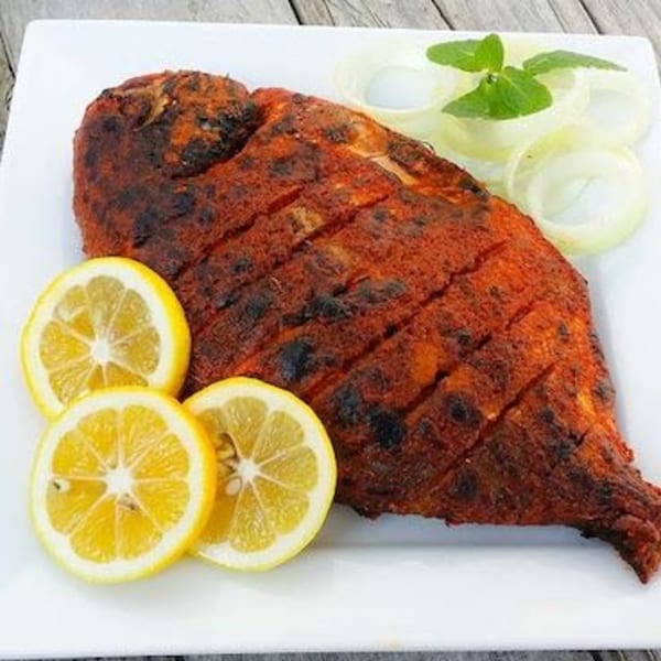 A whole grilled Indian fish, garnished with lemon slices, onion rings, and mint leaves.
